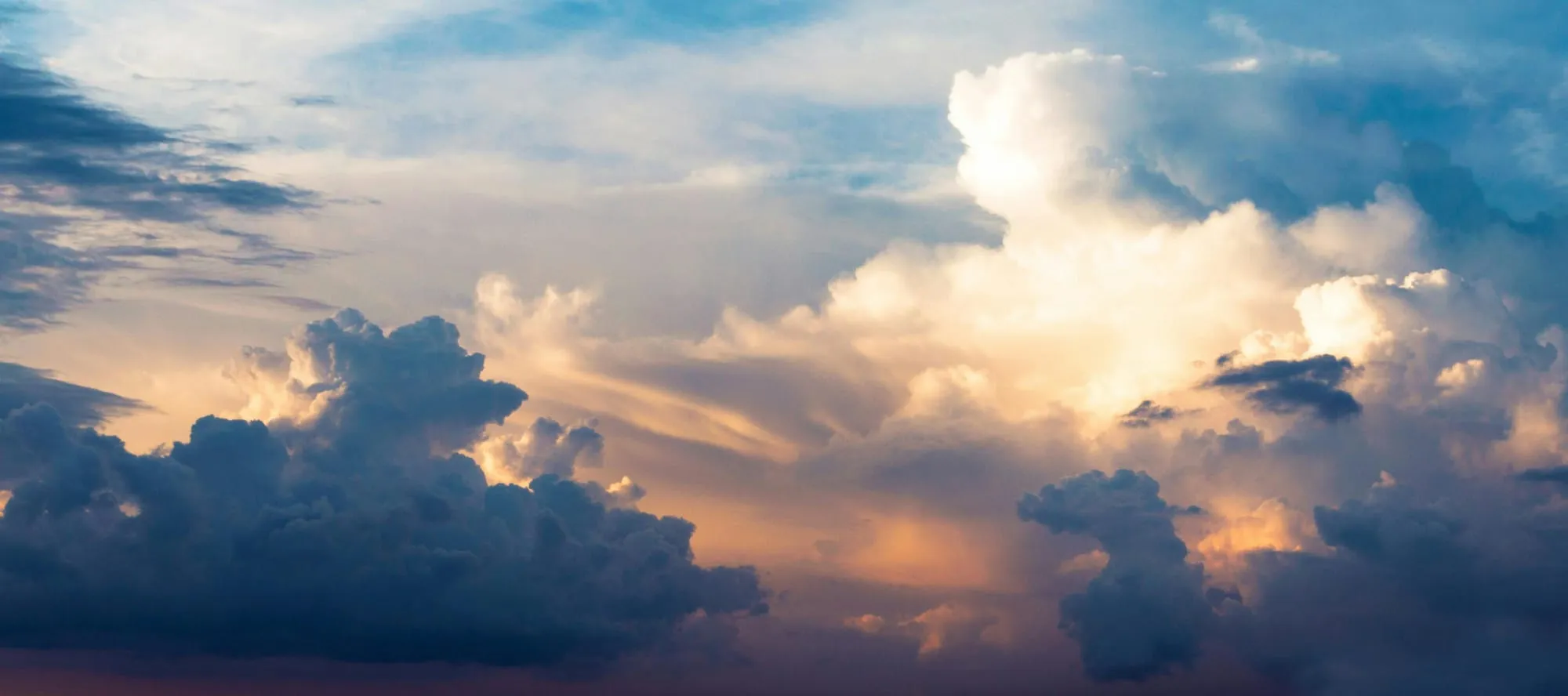 A photo of cumulus clouds with the orange tinge of a nearby sunset.